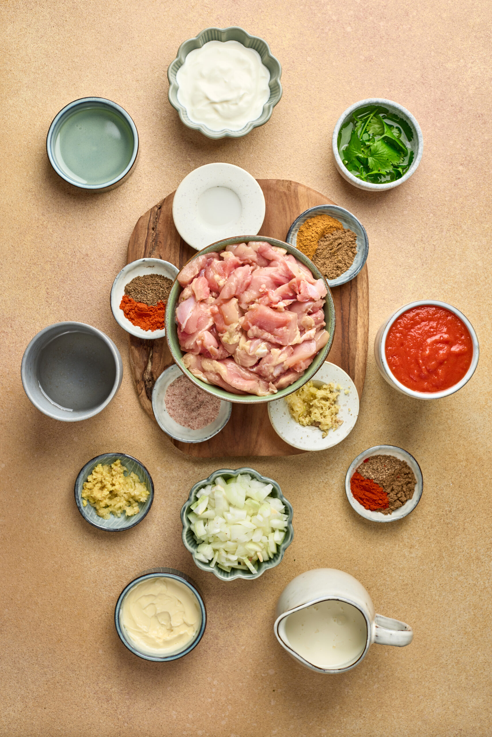 Butter Chicken ingredients including yogurt, chicken, tomato puree, spices, and cream arranged on a kitchen counter.