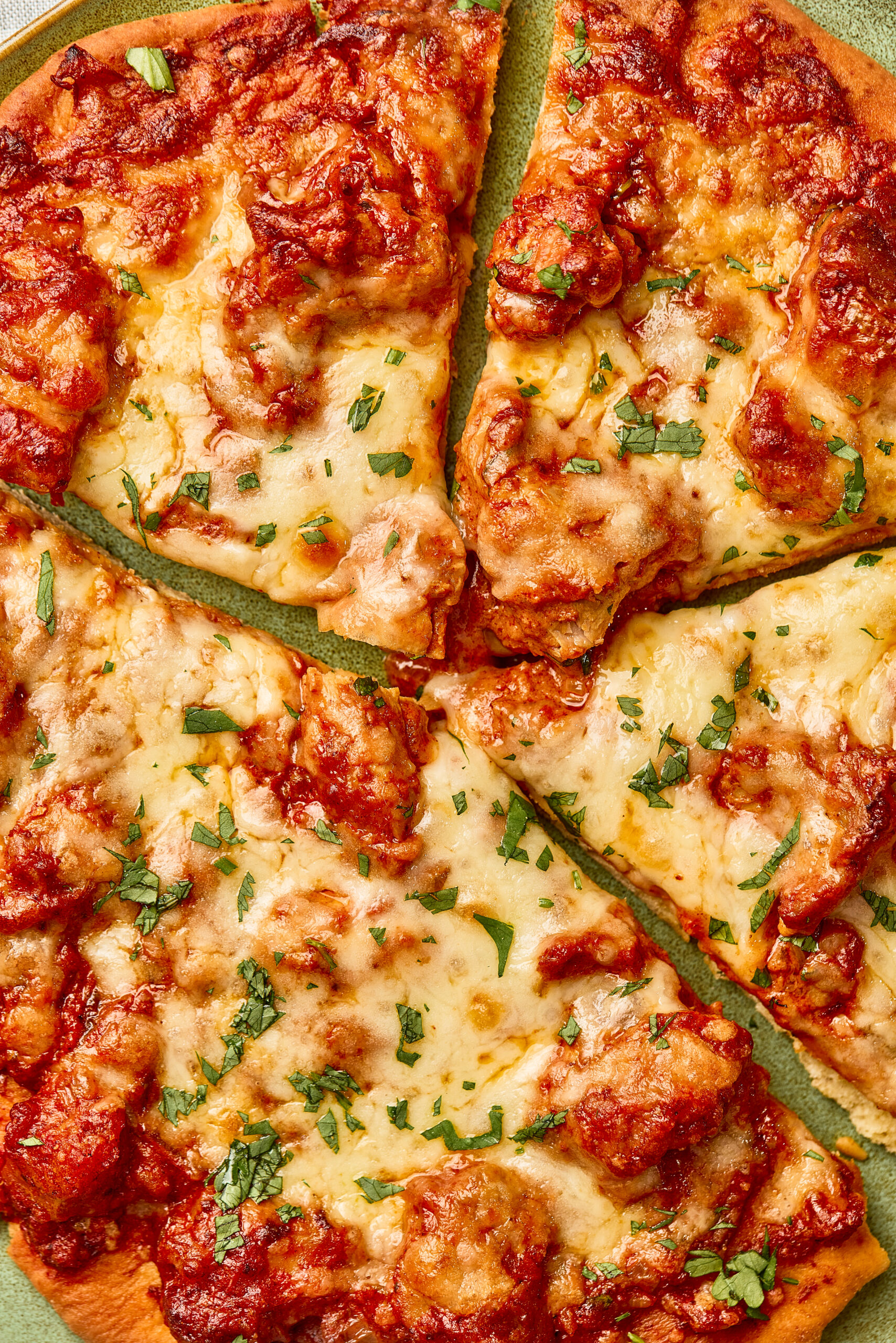 Close-up of Butter Chicken Pizza showing creamy tomato sauce under melted cheese and tender chicken pieces.