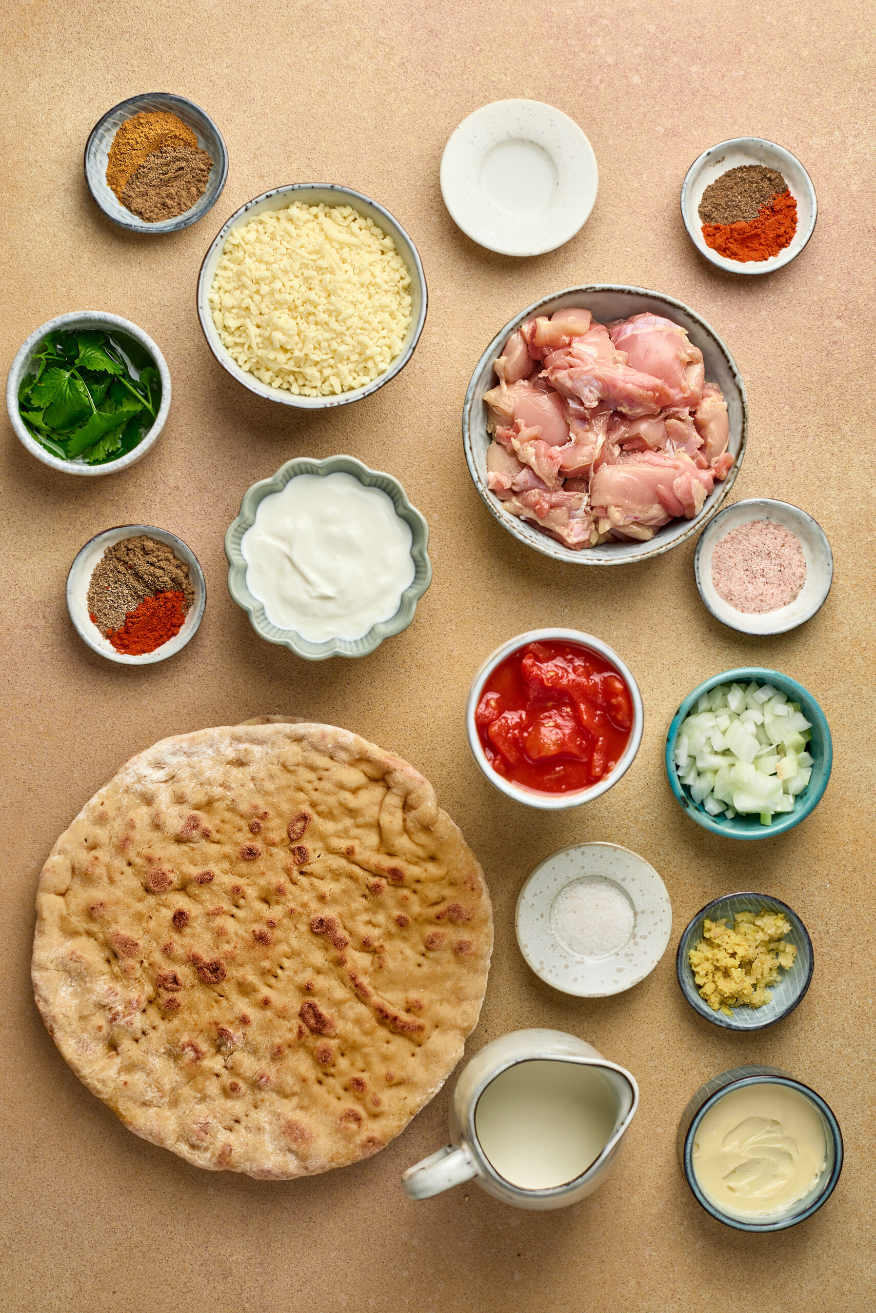Ingredients for Butter Chicken Pizza including pizza dough, butter chicken, cheese, onions, and bell peppers arranged on a counter.