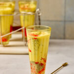 Falooda served in a tall glass with rose syrup, basil seeds, vermicelli, milk, and a scoop of vanilla ice cream topped with nuts