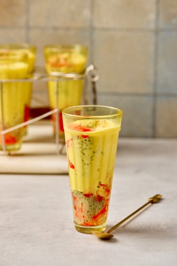 Falooda served in a tall glass with rose syrup, basil seeds, vermicelli, milk, and a scoop of vanilla ice cream topped with nuts