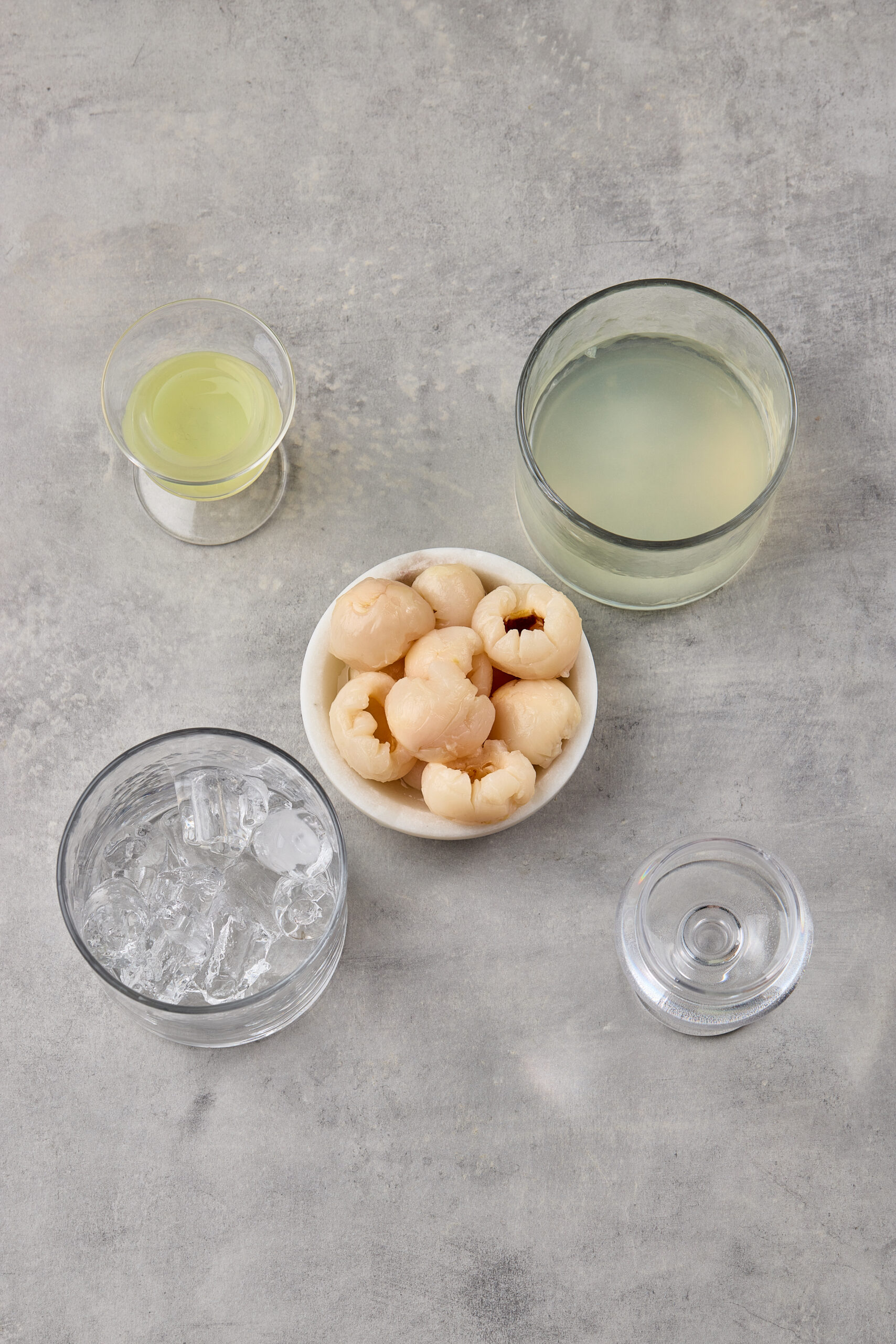 Ingredients for Lychee Martini including vodka, canned lychees, lime, and Cointreau arranged on a bar counter.