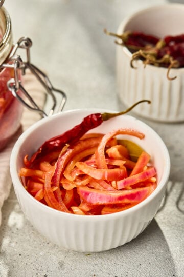 Bright pickled red onions in a white bowl, tangy vinegar brine onions served as a condiment for tacos, salads, and curries
