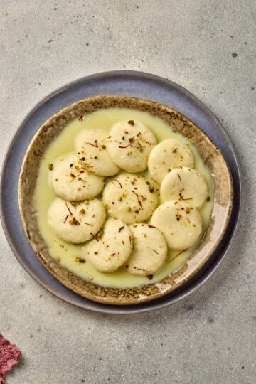 Ras Malai served in a bowl with saffron milk, garnished with pistachios and almonds.
