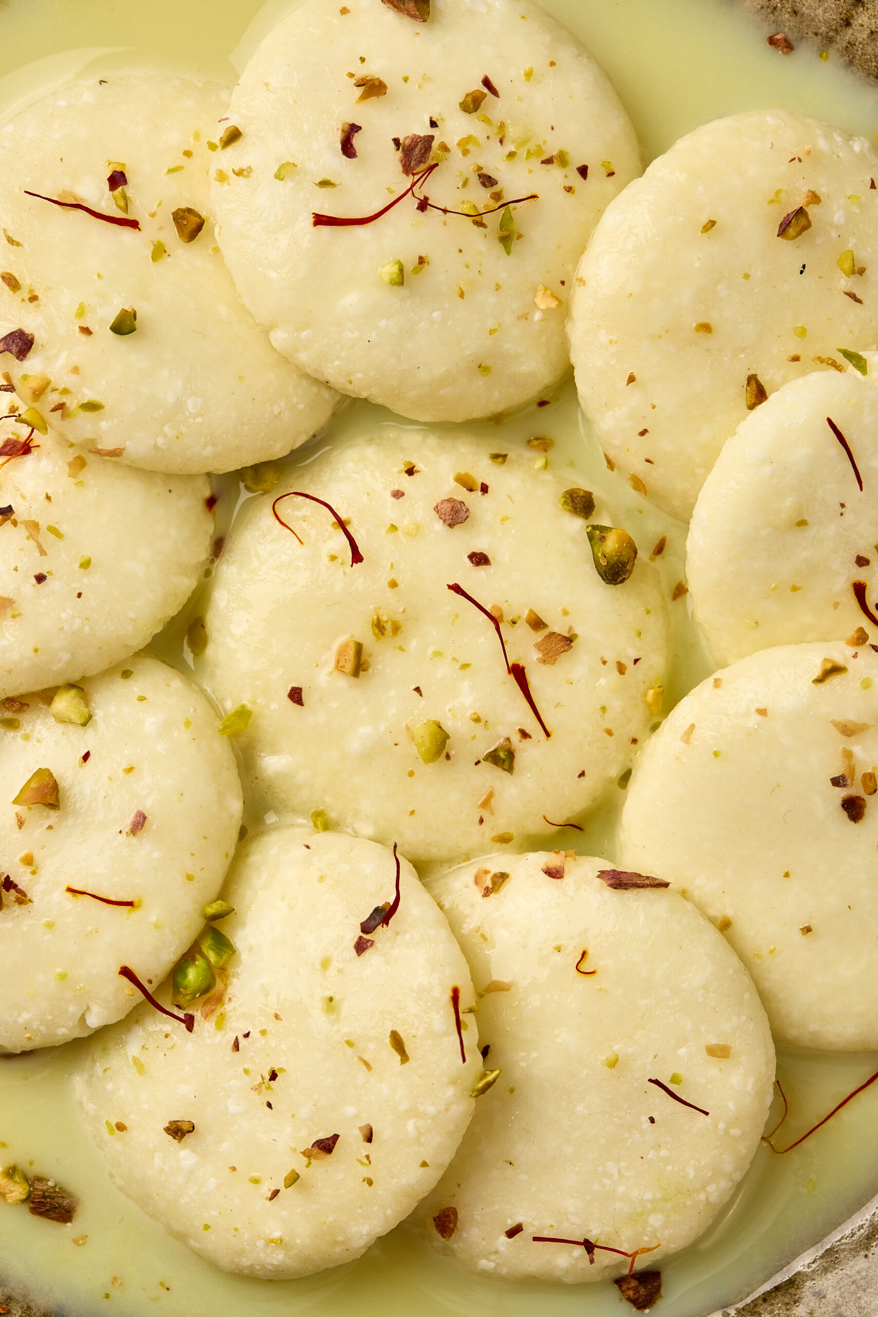 Close-up of Ras Malai showing spongy paneer dumplings soaked in creamy saffron milk.