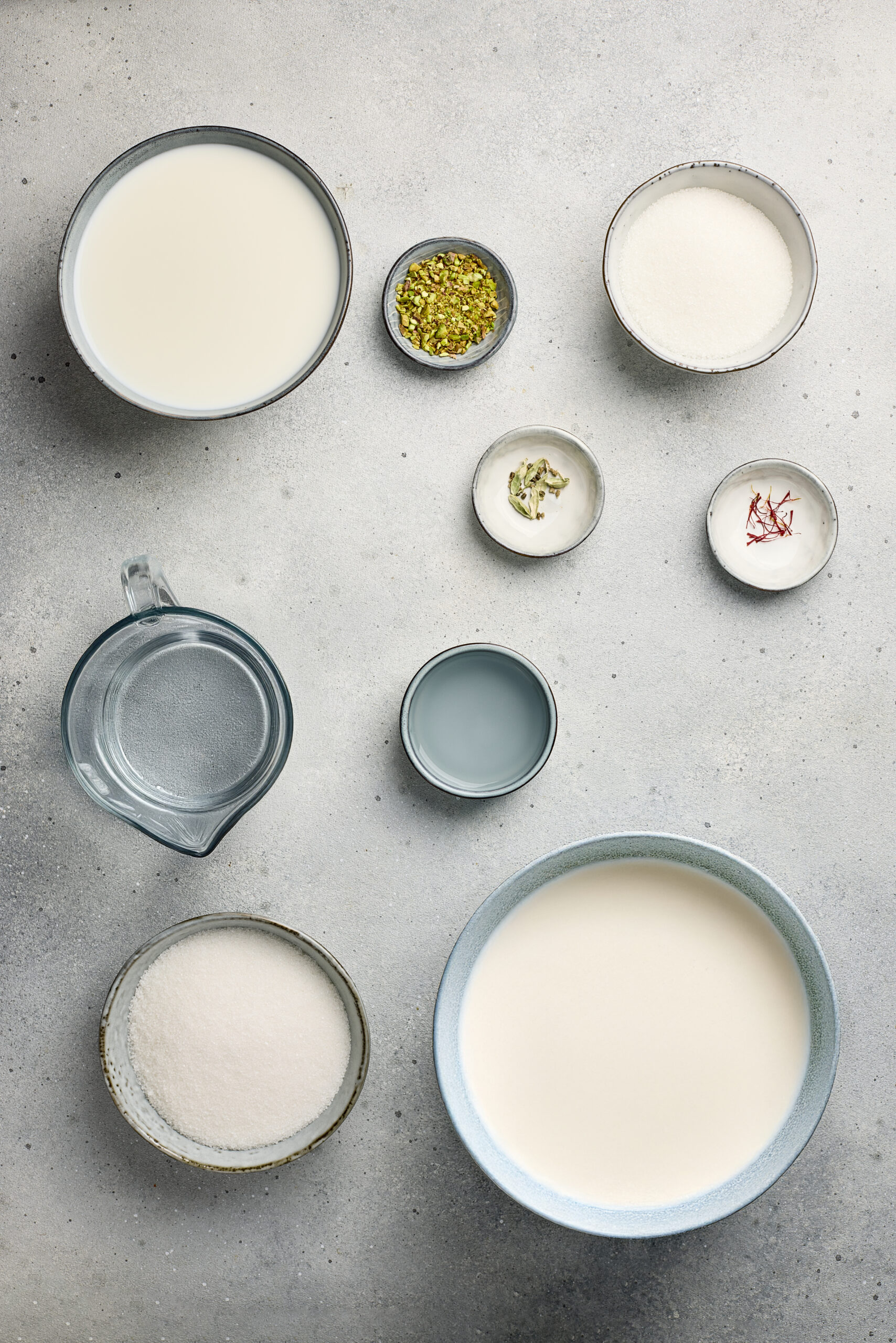 Ingredients for Ras Malai including milk, saffron, sugar, cardamom, and paneer arranged on a kitchen counter.