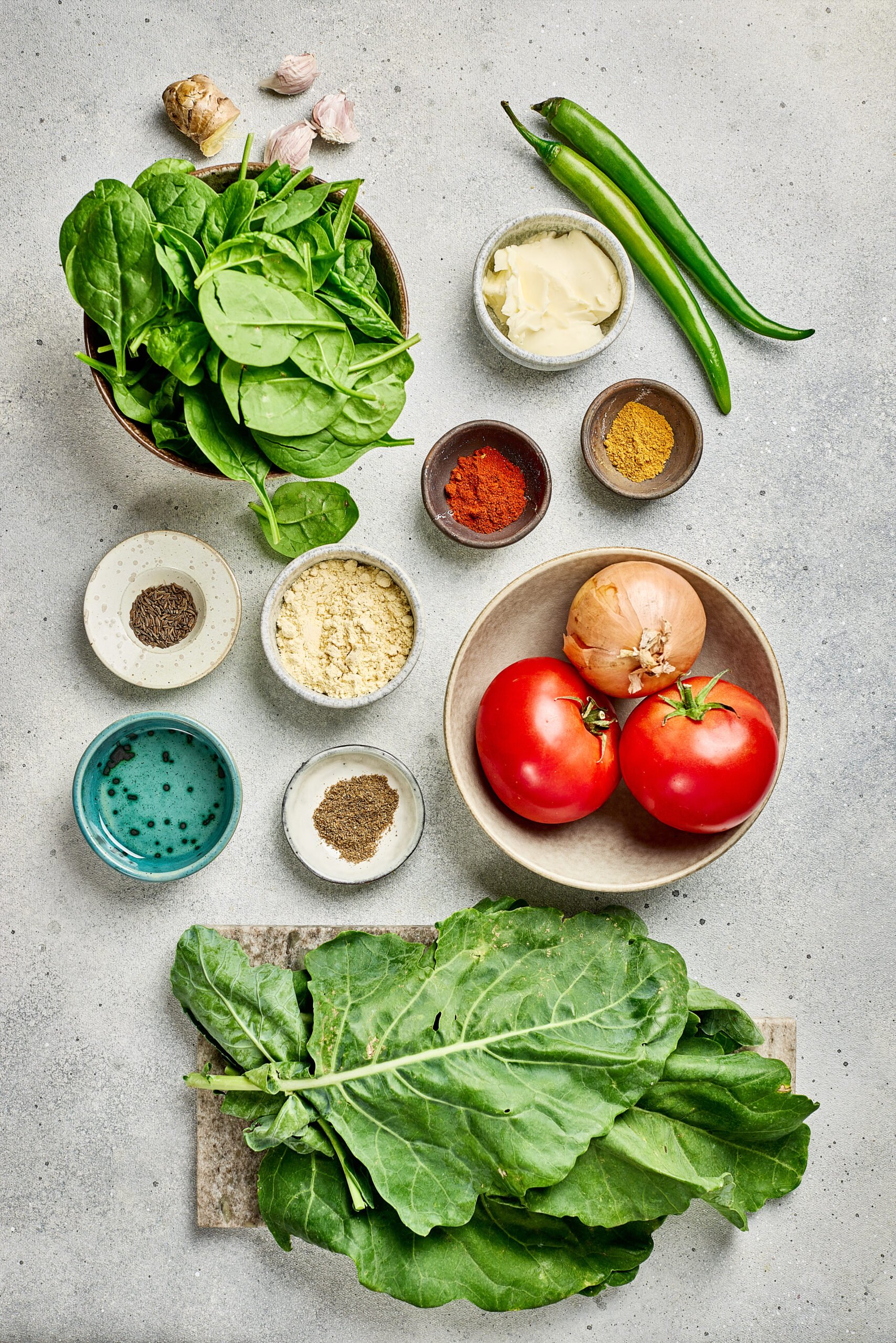 Ingredients for Saag including mustard greens, spinach, onions, tomatoes, spices, and maize flour arranged on a counter.