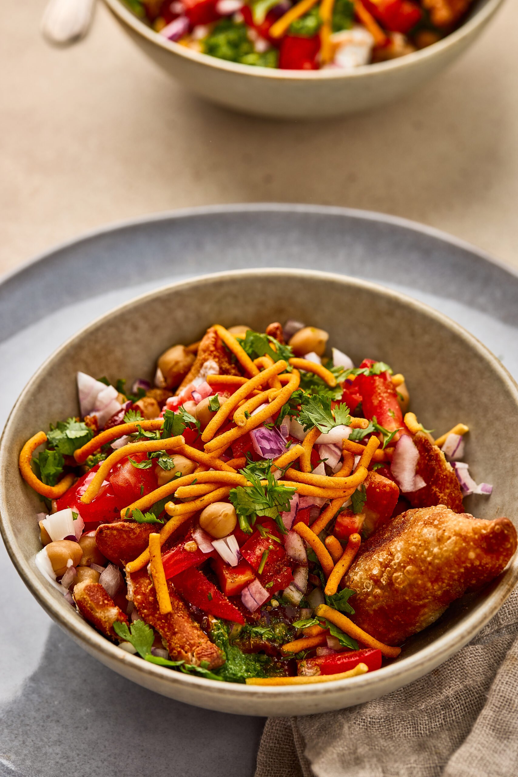 Close-up of Samosa Chaat showing layers of crispy samosa, onions, tomato and coriander leaves.