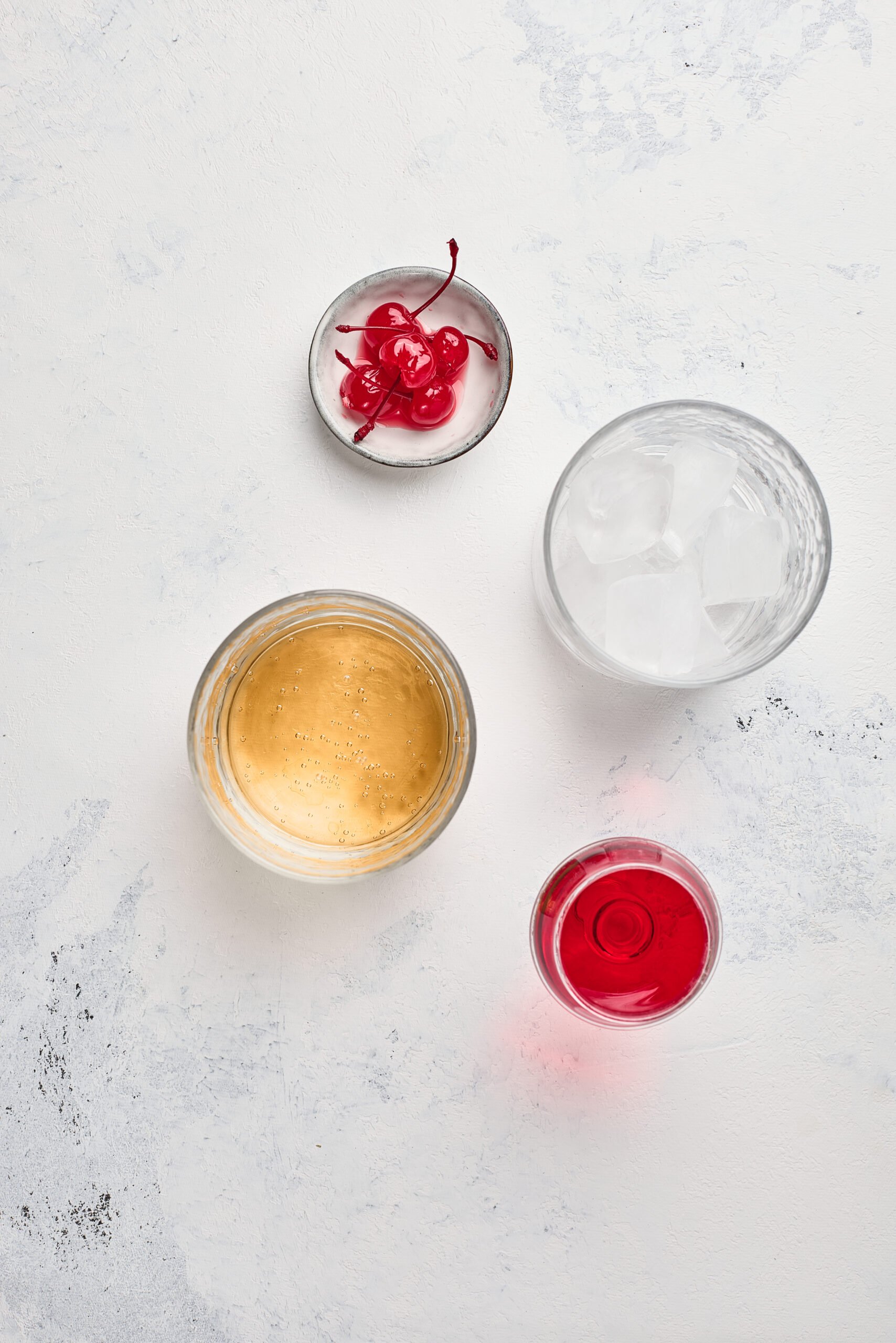 Ingredients for Shirley Temple Drink including ginger ale, grenadine, lime, and maraschino cherries on a counter.