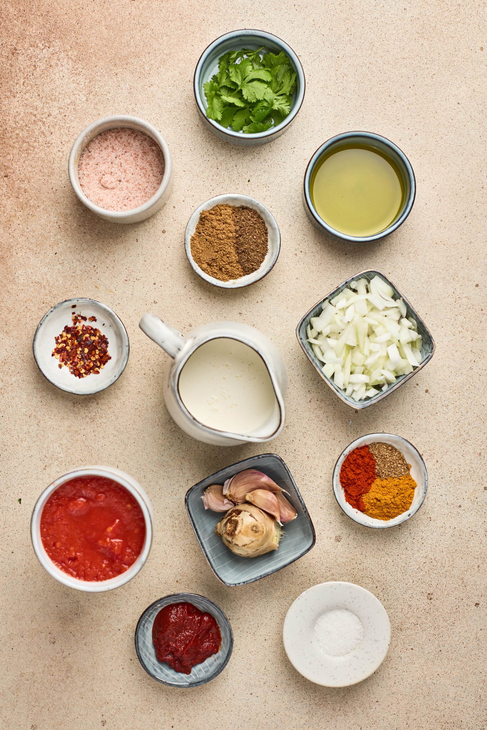 Ingredients for Tikka Masala Sauce including onion, tomato puree, cream, and ground spices arranged on a kitchen counter.