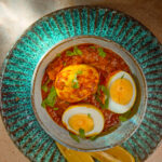 Egg Pulusu served in a clay bowl with boiled eggs in tangy tamarind gravy, garnished with coriander.
