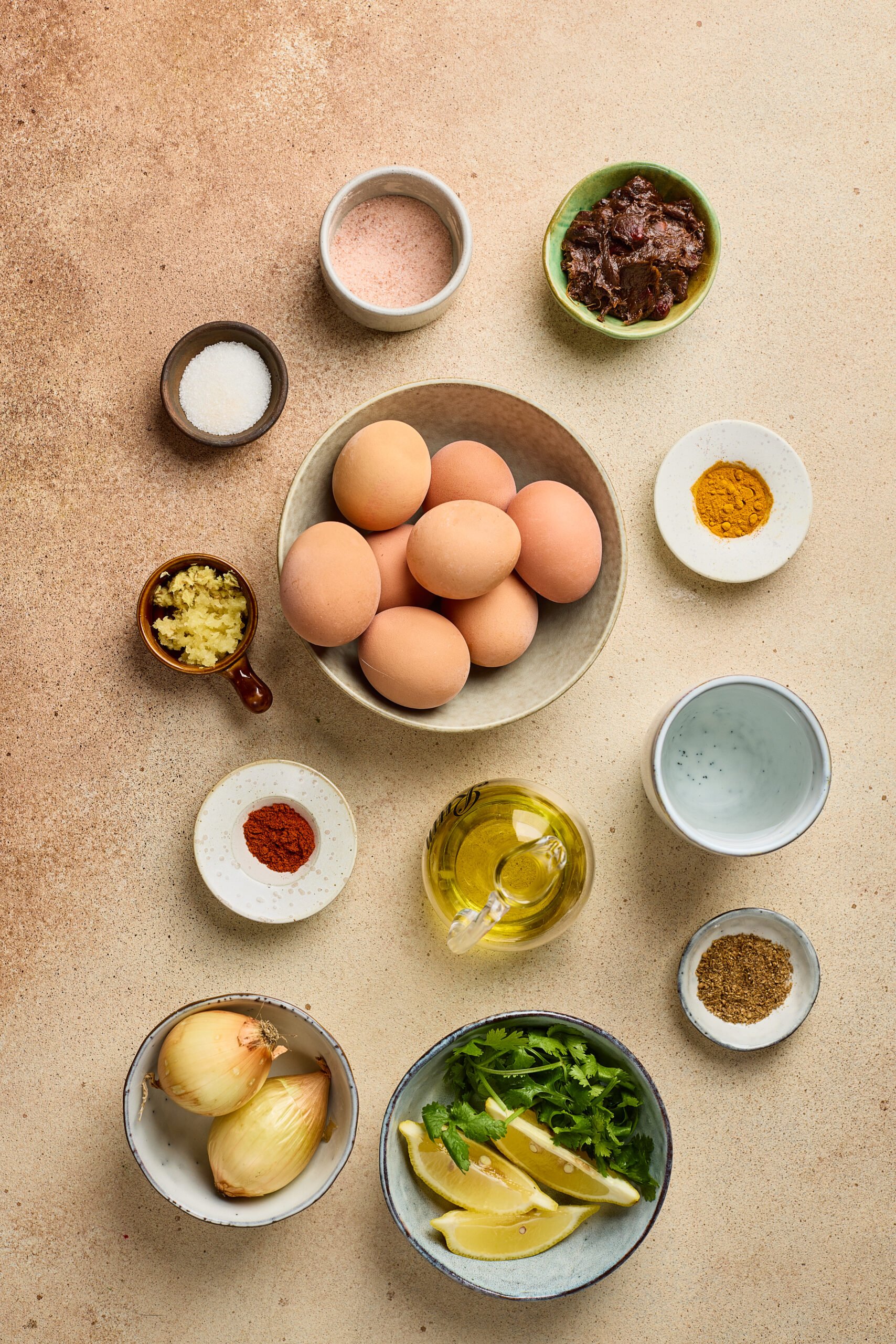 Ingredients for Egg Pulusu including boiled eggs, tamarind pulp, onions, tomatoes, curry leaves, and spices arranged on a counter.
