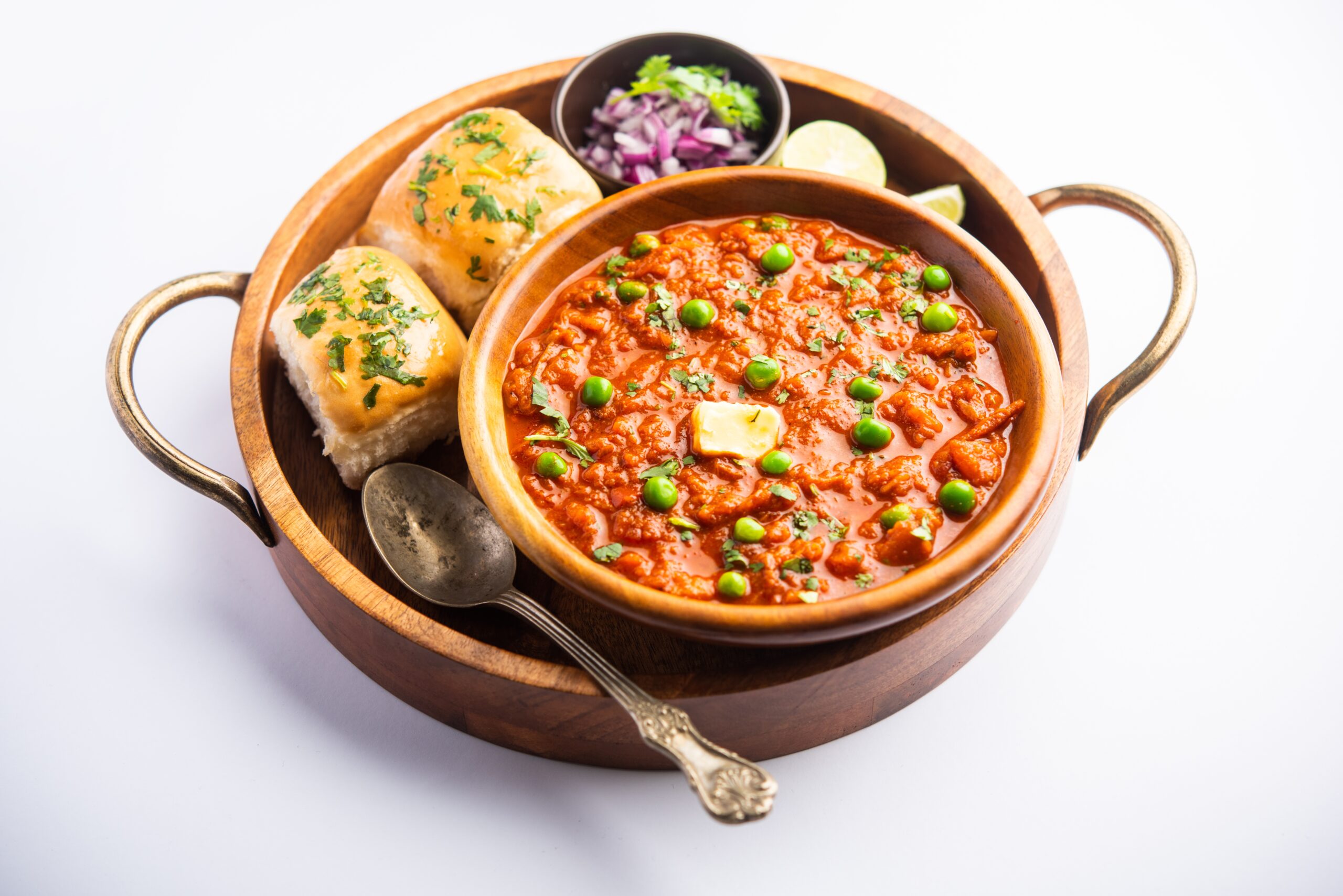 Pav bhaji served with soft buttered buns, onions, fresh coriander, and lemon wedges for garnish.