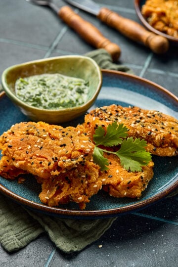 Sesame-Crusted Paneer Fingers served on a platter with golden crust and dipping sauce on the side.