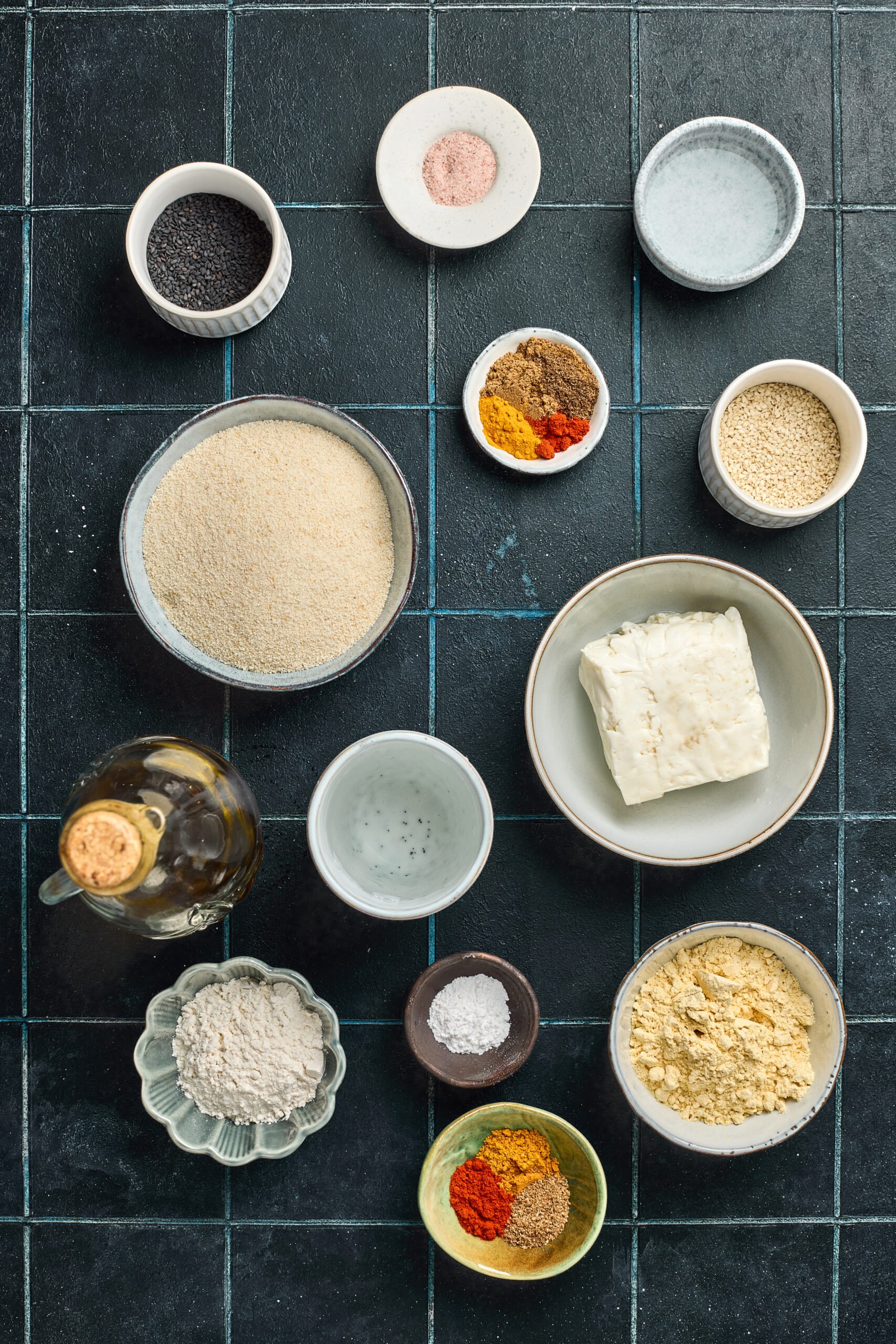 Ingredients for Sesame-Crusted Paneer Fingers including paneer strips, sesame seeds, flour, cornstarch, chili powder, salt, and oil arranged on a kitchen counter.