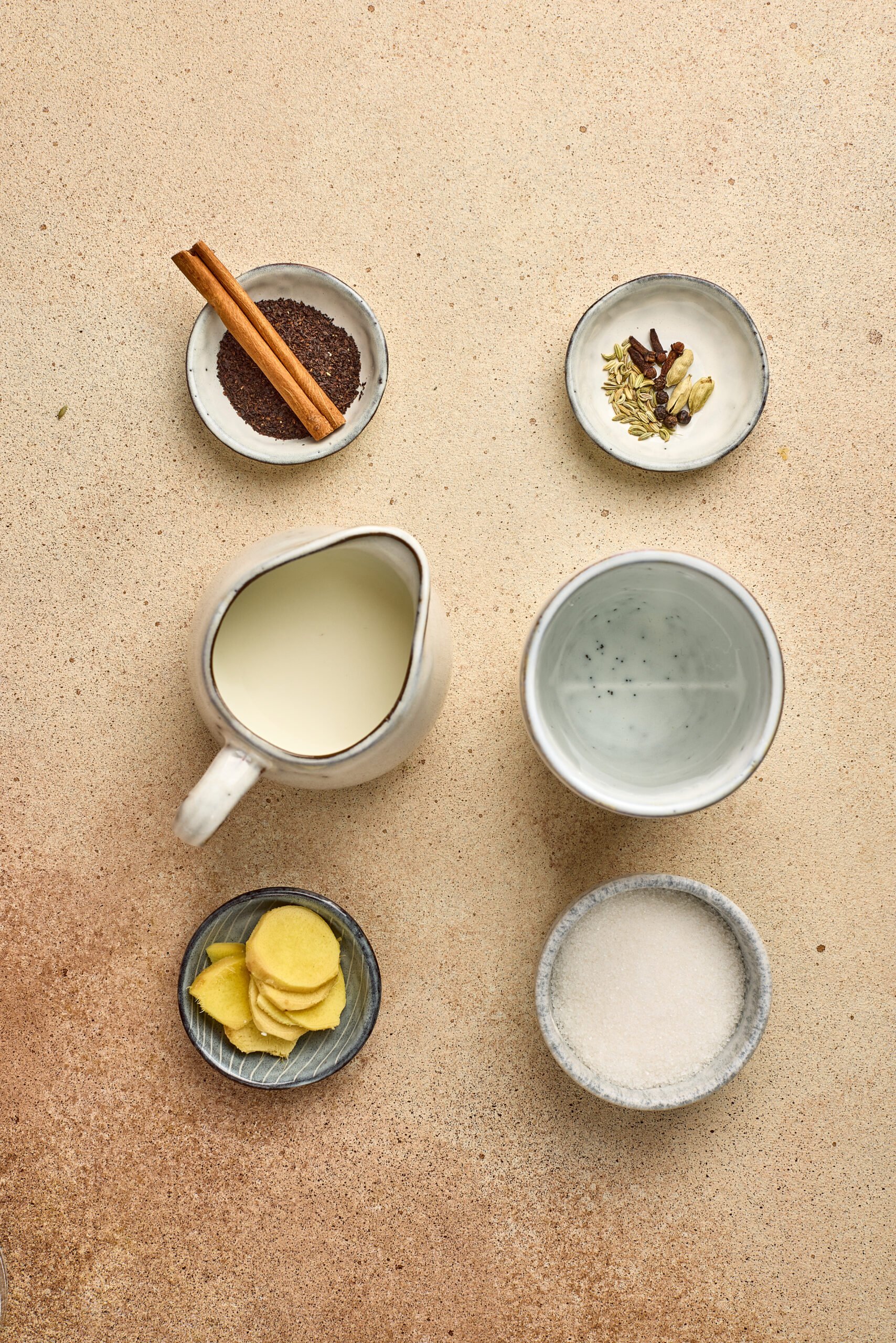 Ingredients for Wagh Bakri Masala Tea Copycat including black tea leaves, cardamom, cloves, cinnamon, ginger, and milk arranged on a counter.