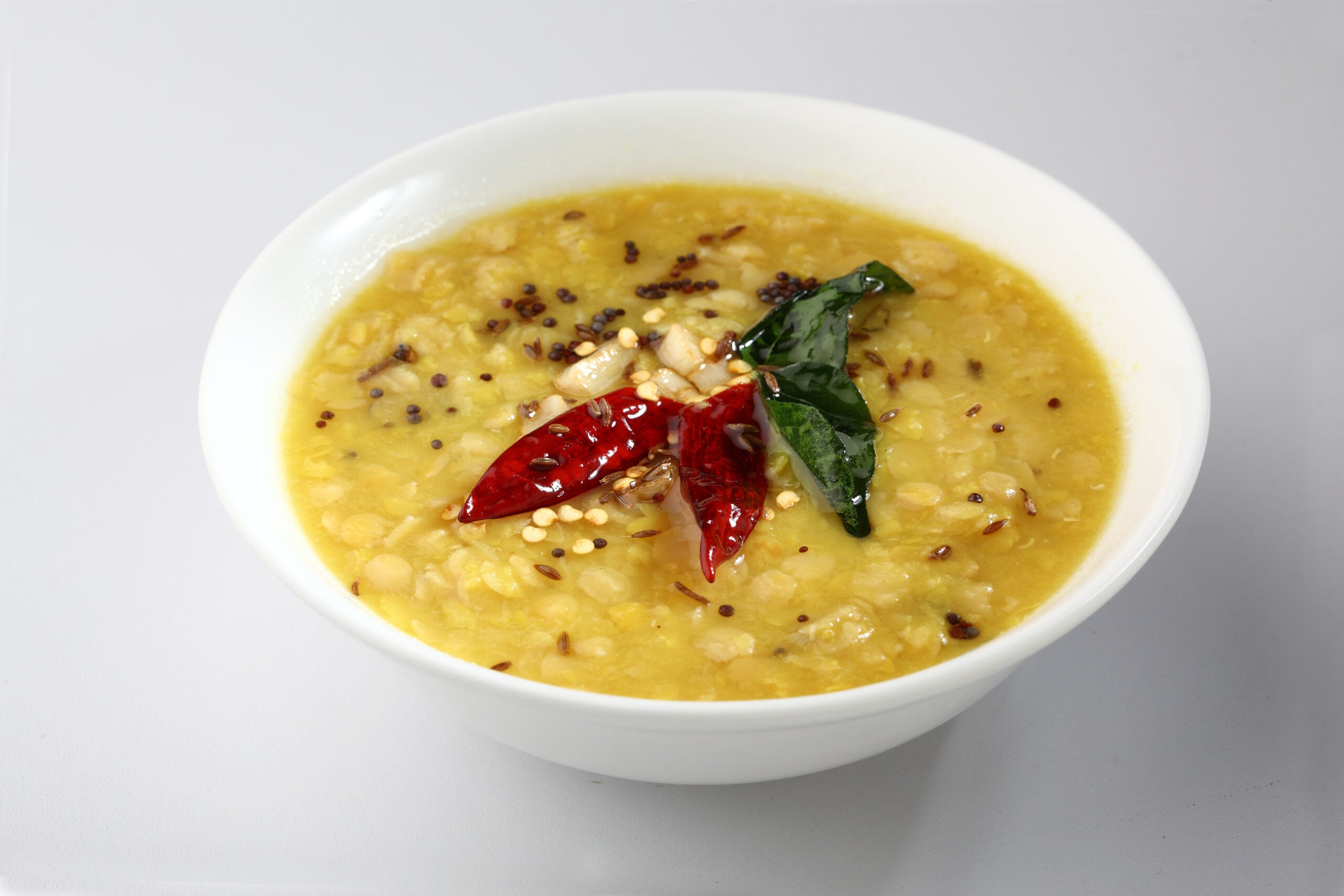 Bowl of chana dal with yellow split chickpeas topped with dried red chili, mustard seeds, and curry leaves